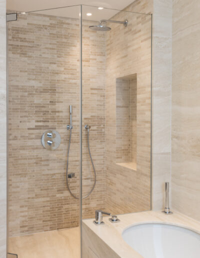 Walk-in shower in Travertine Bianco with recessed niche and frameless glass enclosure London